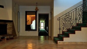 Un hall d’entrée spacieux avec une cheminée, un escalier orné de balustrades travaillées et une vue sur une autre pièce.
