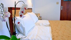 Une chambre d’hôtel avec un lit, du linge de lit blanc, une tête de lit en bois et un pot d’orchidée.