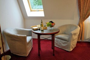 A room with two white armchairs, a small round table with a bottle, glasses, and a fruit bowl. - Dwor Wapowce (Przemysl)