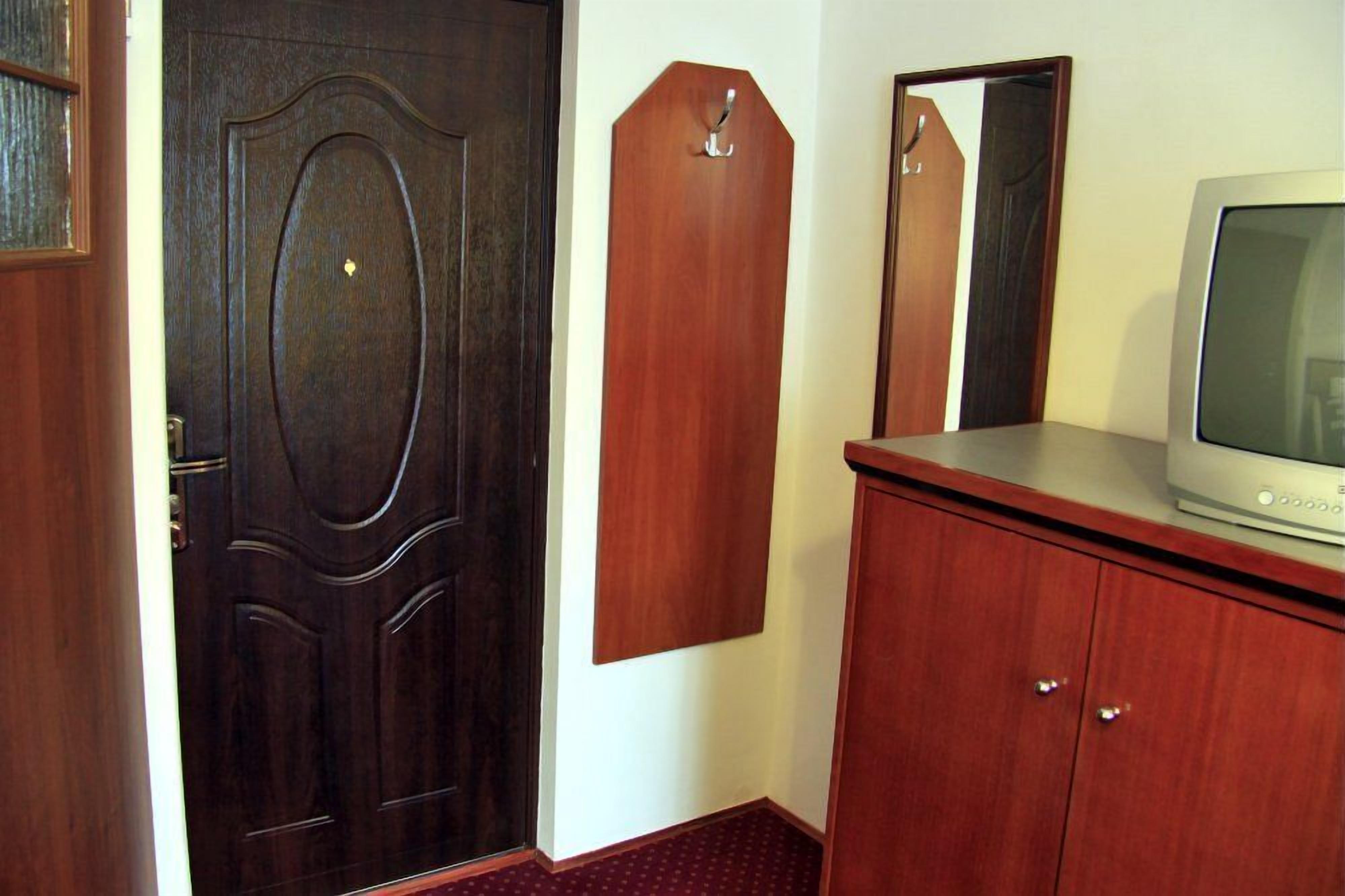 Een kamer met een donkerhouten deur, een houten kapstok, een televisie op een houten kast en een spiegel aan de muur.