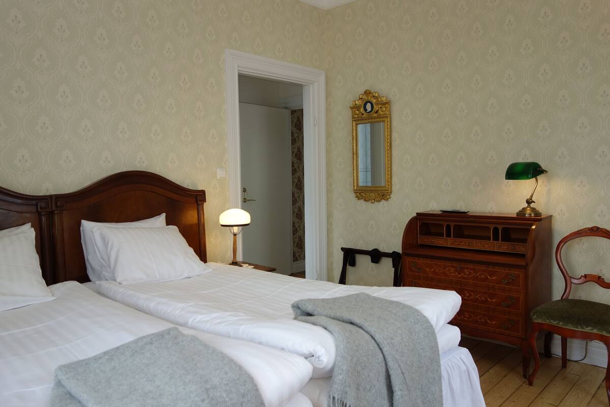 A hotel room with two beds, a dresser, a mirror, and a lamp.