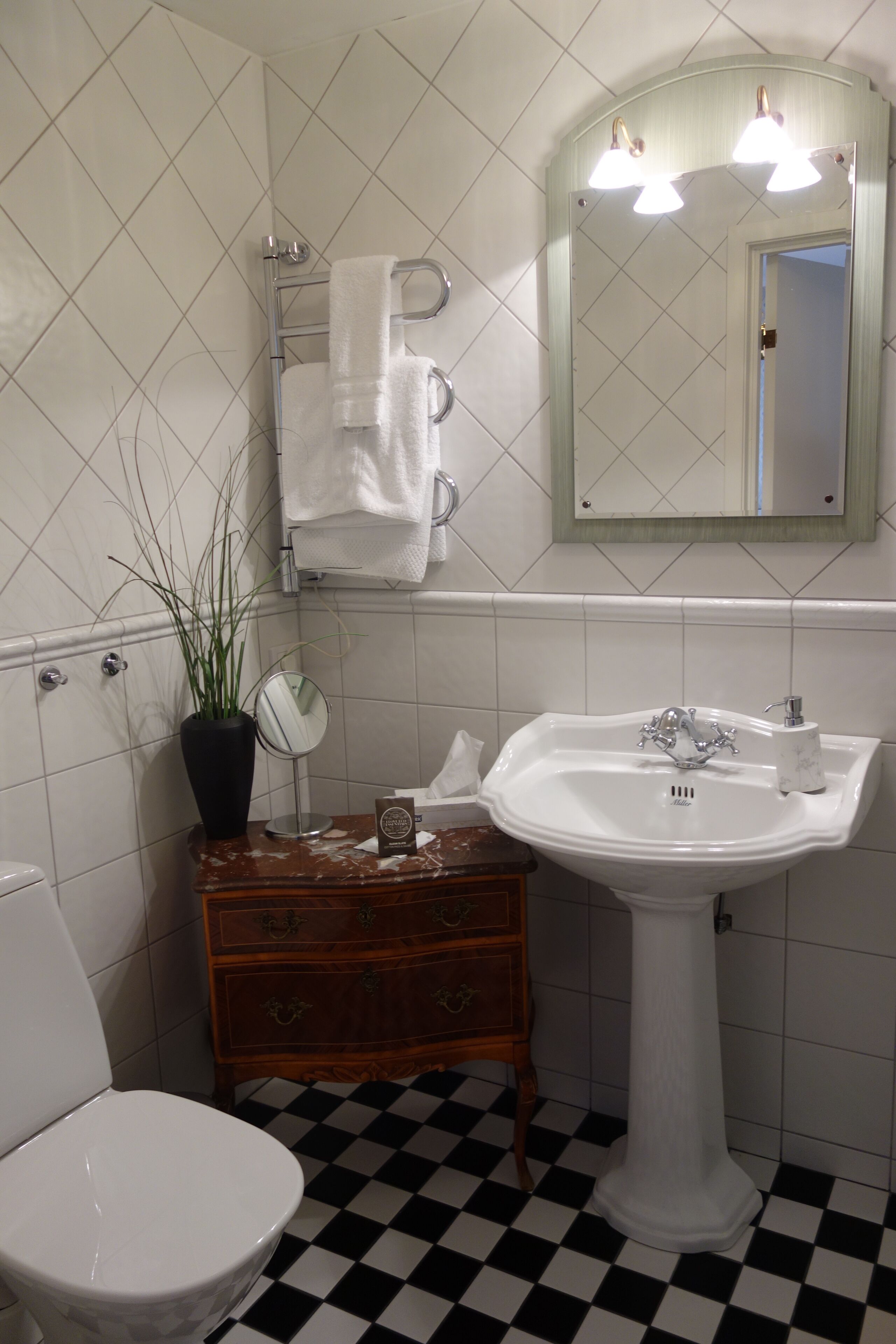 A bathroom with a white sink, a mirror, a towel rack, a potted plant, and a checkered floor.