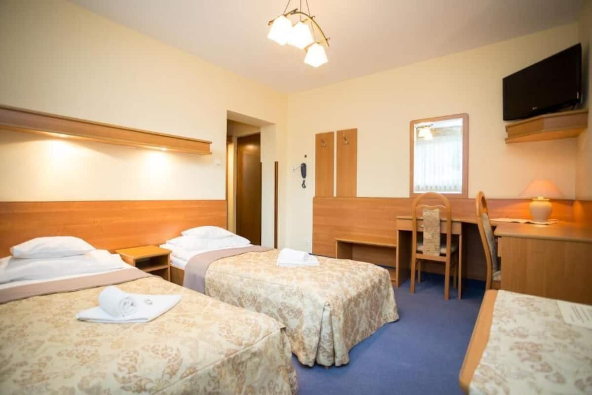 Ein Hotelzimmer mit zwei Betten, einem Schreibtisch, einem Sessel, einem Fernseher und einem Telefon.