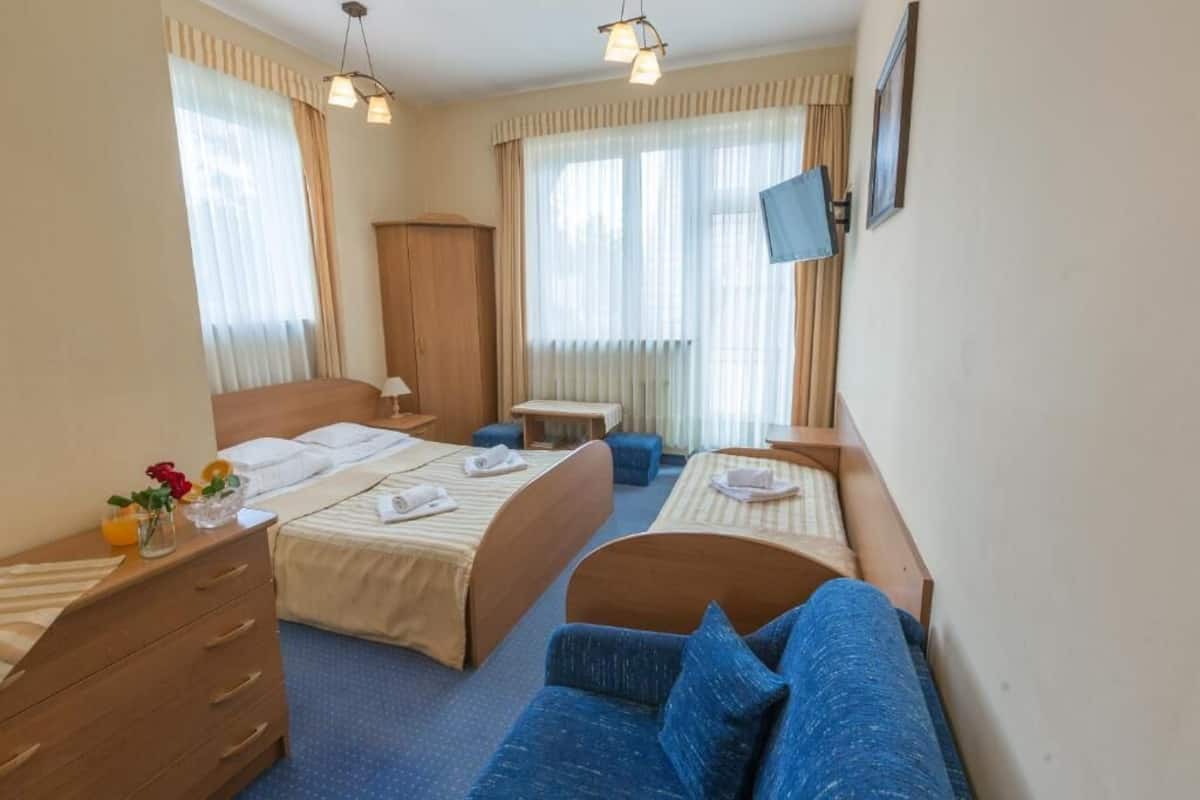 Ein Hotelzimmer mit zwei Betten, einer Schlafcouch, einem Schreibtisch und einem Fernseher.