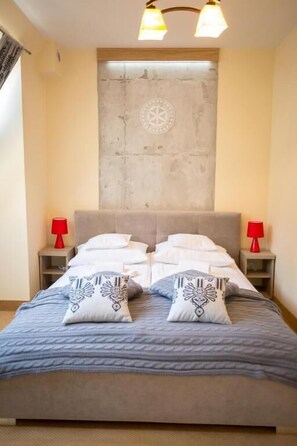 A bed with a grey blanket and two pillows, two bedside tables with red lamps, a concrete wall with a circular design, and a ceiling light fixture. - Ośrodek Usług Hotelarsko-Gastronomicznych Fian (Zakopane)