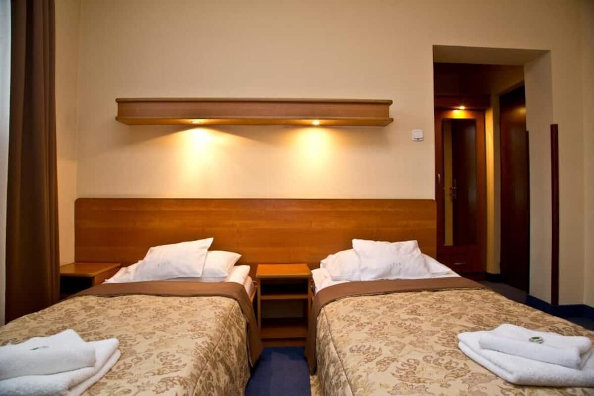 Ein Hotelzimmer mit zwei Betten, einem Holz-Kopfteil, einem Nachttisch und einer Wandleuchte.