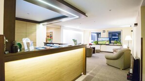 A reception area with a wooden desk, a flat-screen TV, a sofa, and a lamp. - Ośrodek Usług Hotelarsko-Gastronomicznych Fian (Zakopane)