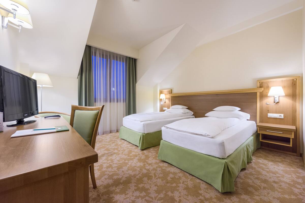 A hotel room with two single beds, a desk with a computer, a chair, and a TV.