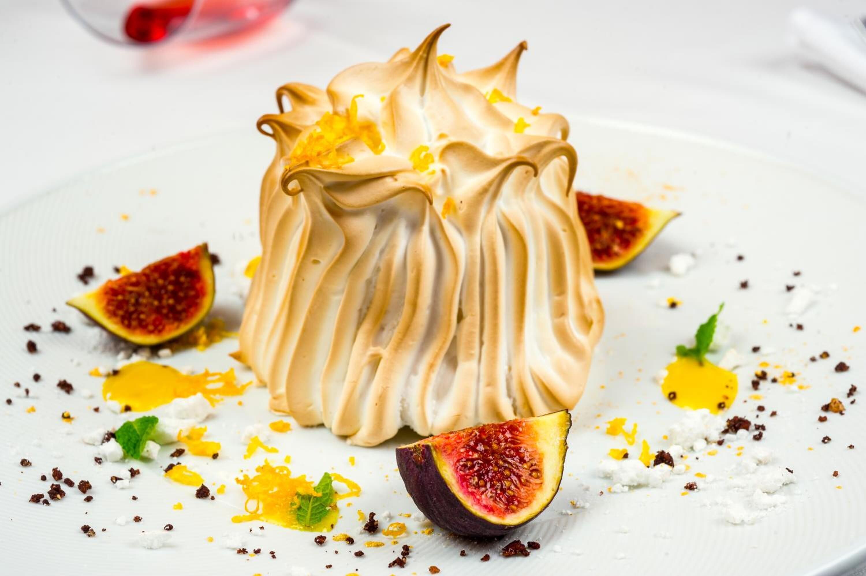 A dessert with a creamy texture, surrounded by figs and scattered with crumbled elements.