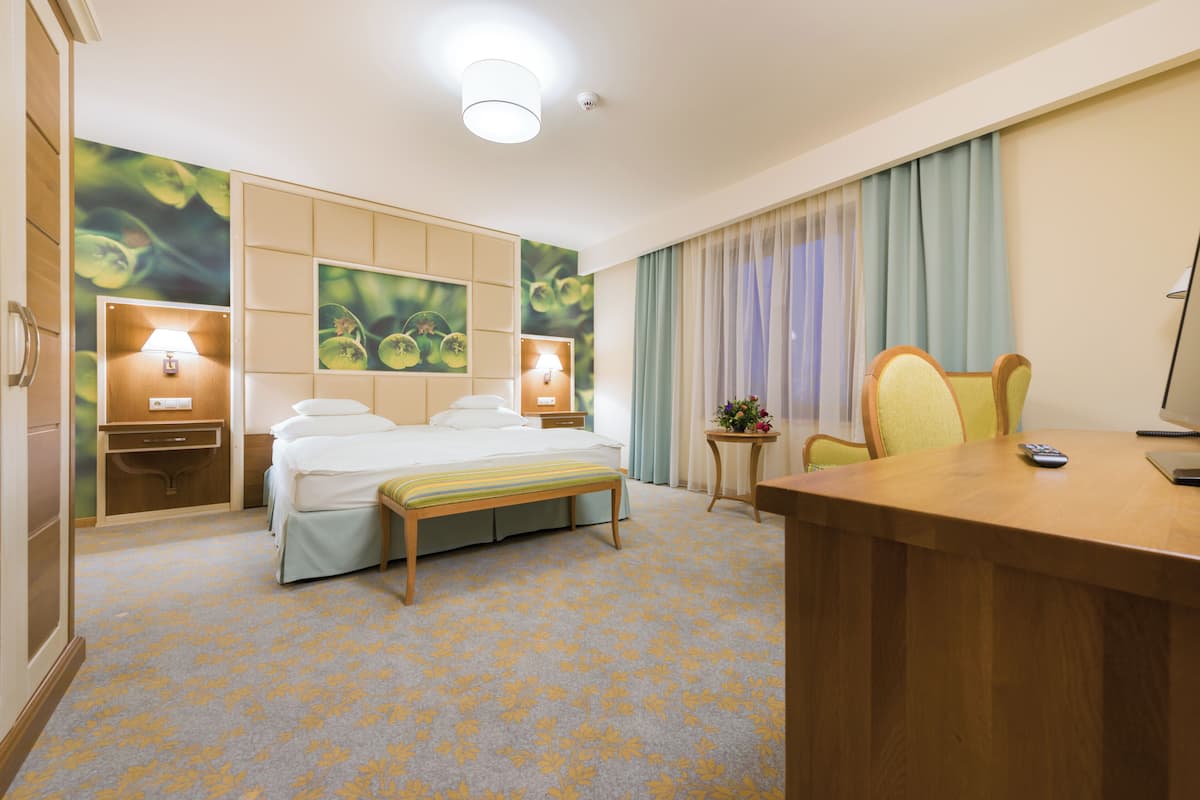 A hotel room with a bed, bedside tables, a desk, and a chair.