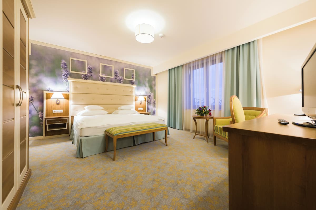 A hotel room with a bed, bedside table, lamp, chair, desk, and a small table with a vase of flowers.