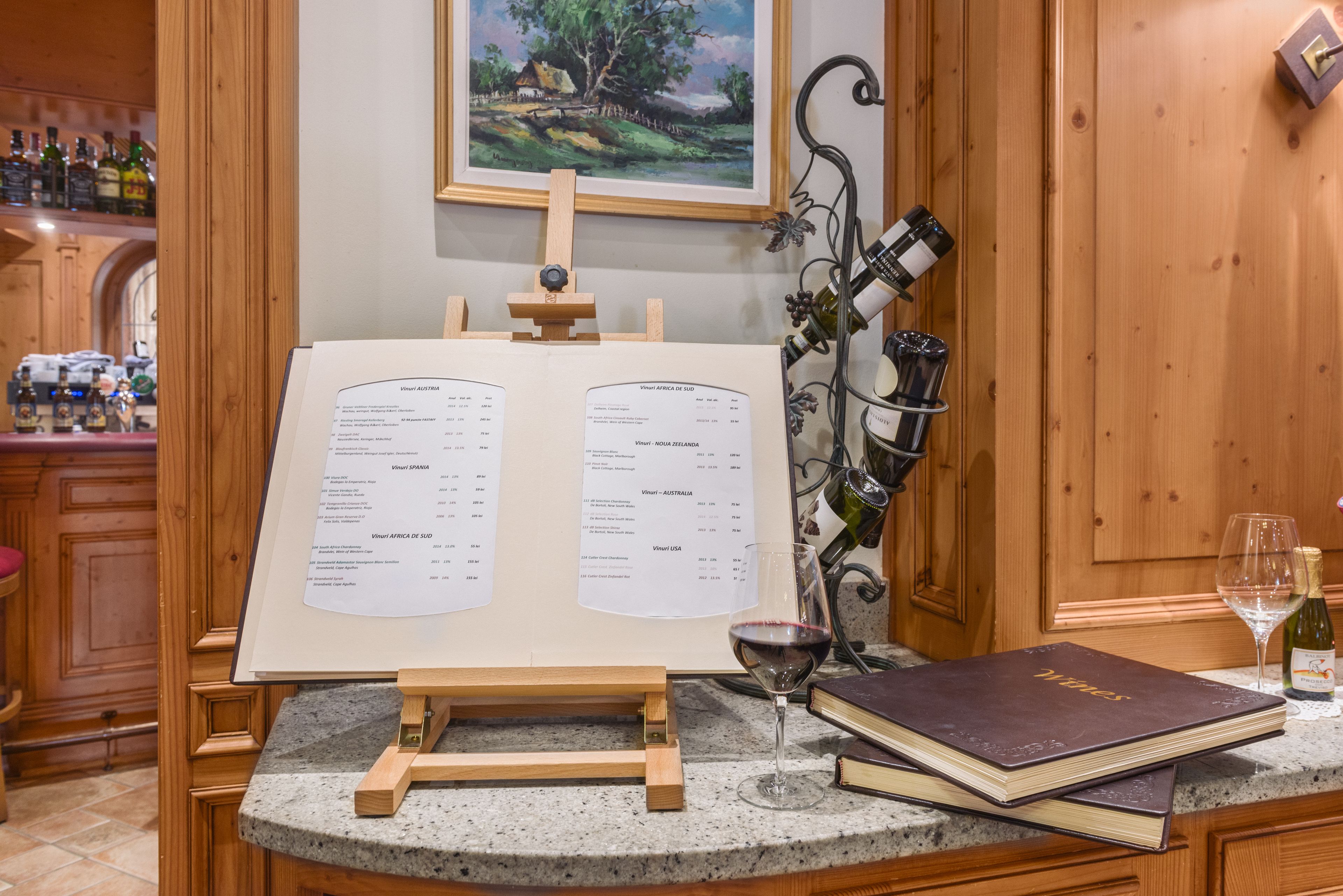 A wine tasting area with an open wine list, a wine glass, and a wine bottle on a counter.