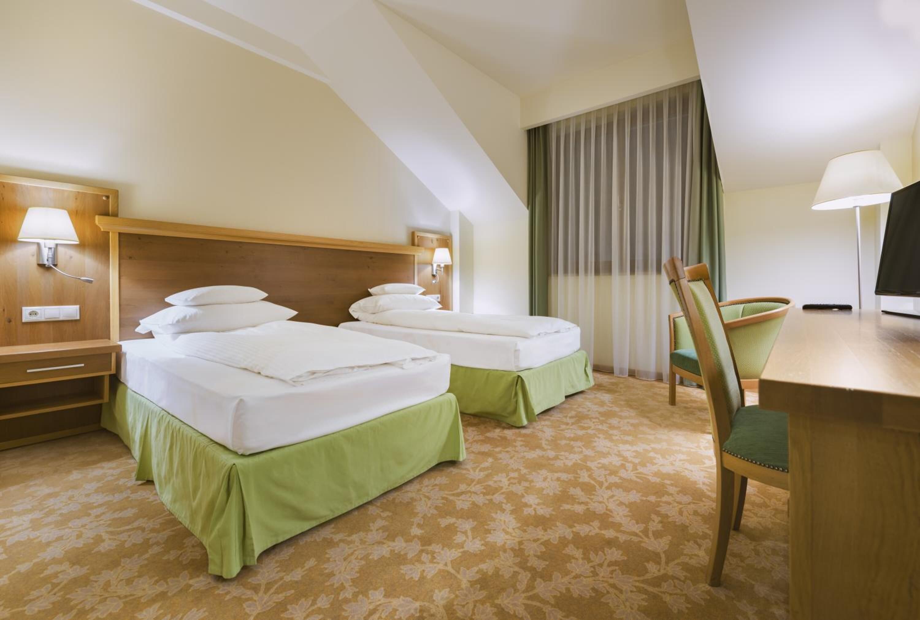 A hotel room with two beds, a desk, a chair, and a television.