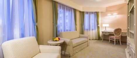 A hotel room with two armchairs, a small round table with fruit, a desk with a lamp, and a wardrobe.