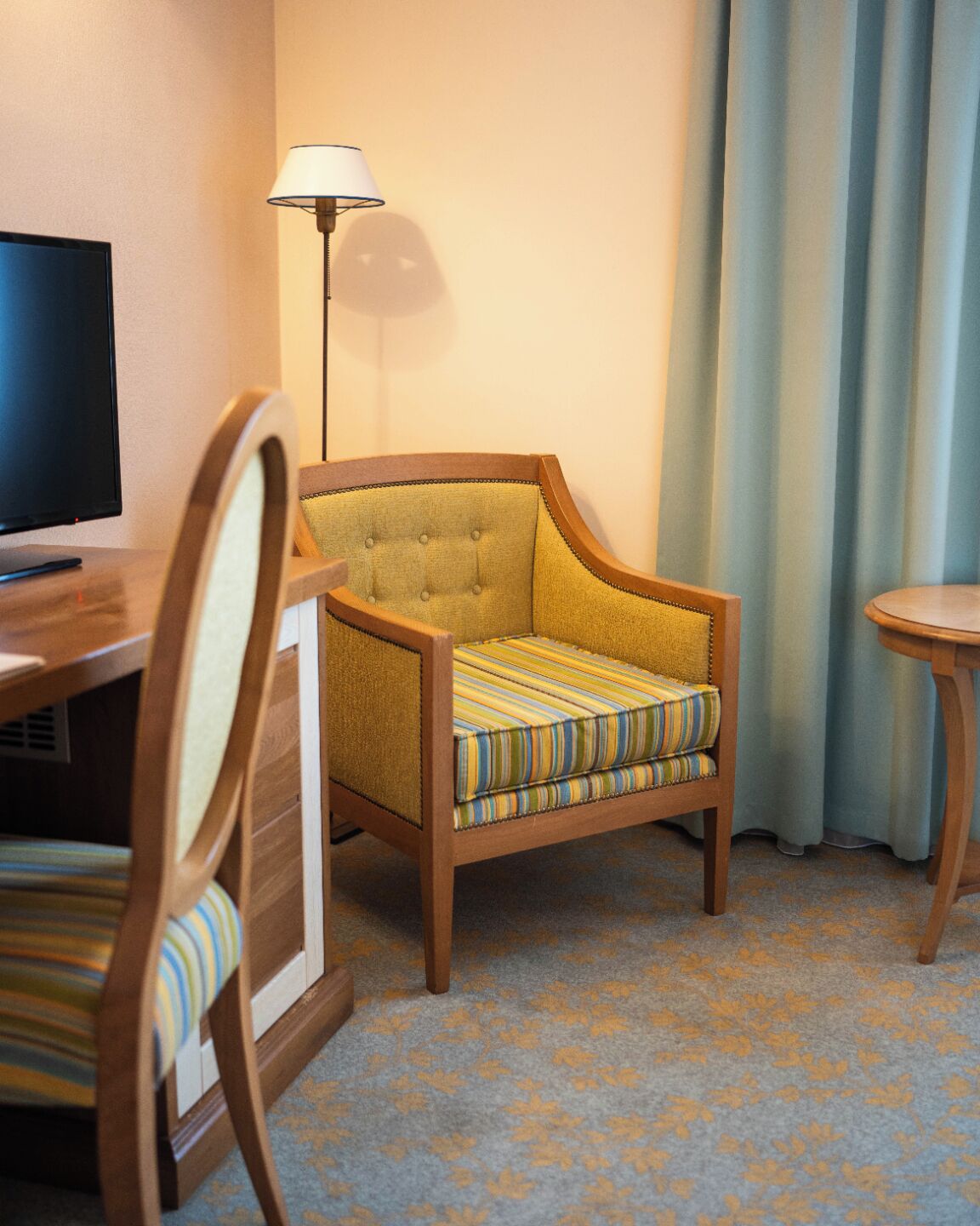 A hotel room with a wooden chair, a television, a lamp, and a small table.