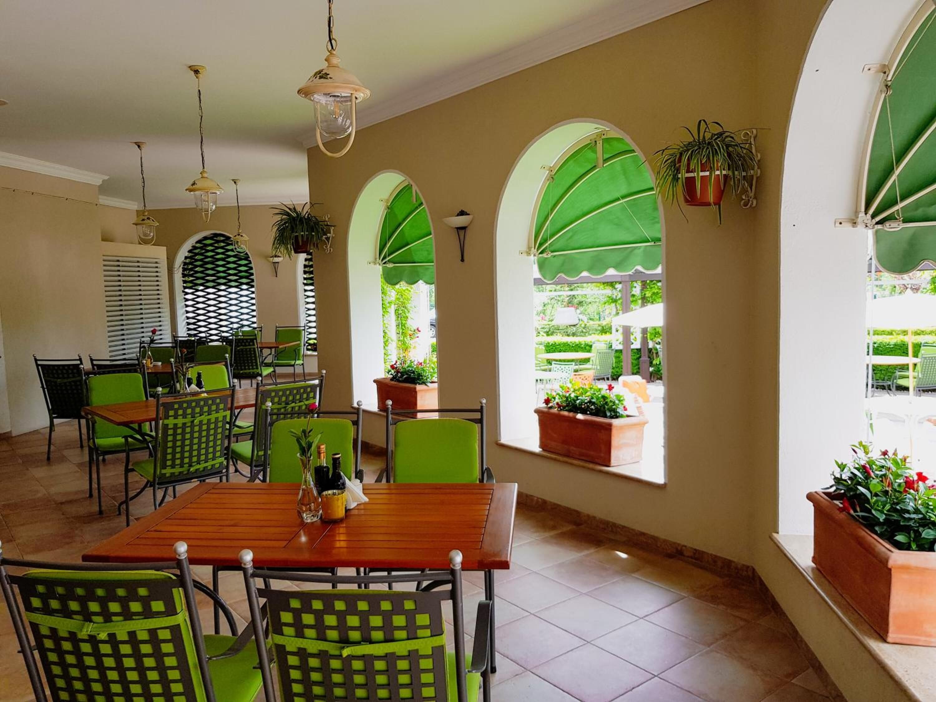 A dining area with green chairs, a wooden table, and a view of the garden through arched windows.