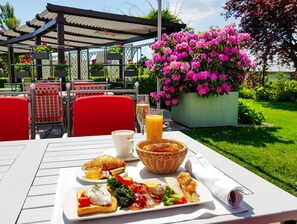 An outdoor dining area with a table set for breakfast, including croissants, toast, and a basket of bread. - Hotel Sonnenhof (Suceava)