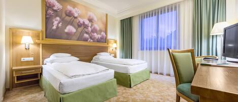 Una habitación de hotel con dos camas, un escritorio, una silla, un televisor y un cuadro grande con motivos florales en la pared.