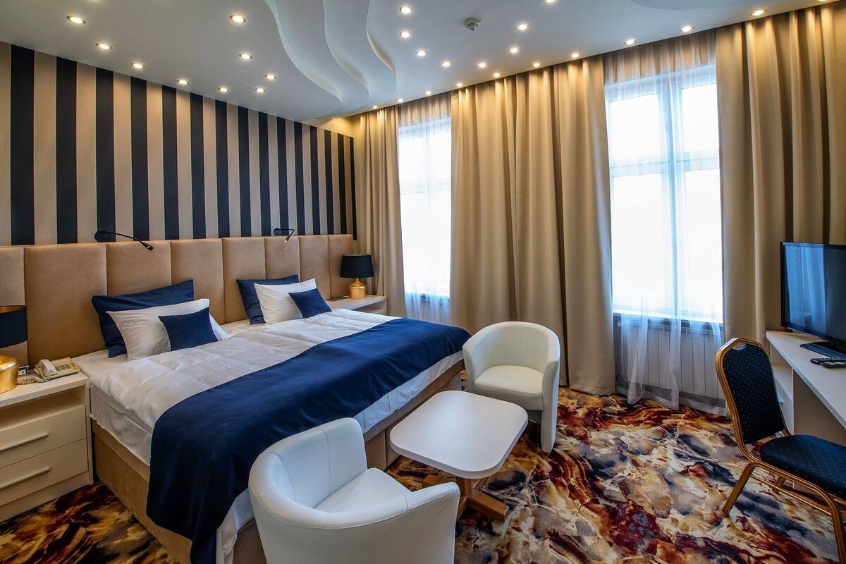 A hotel room with a large bed, a desk with a TV, a chair, and a patterned carpet.