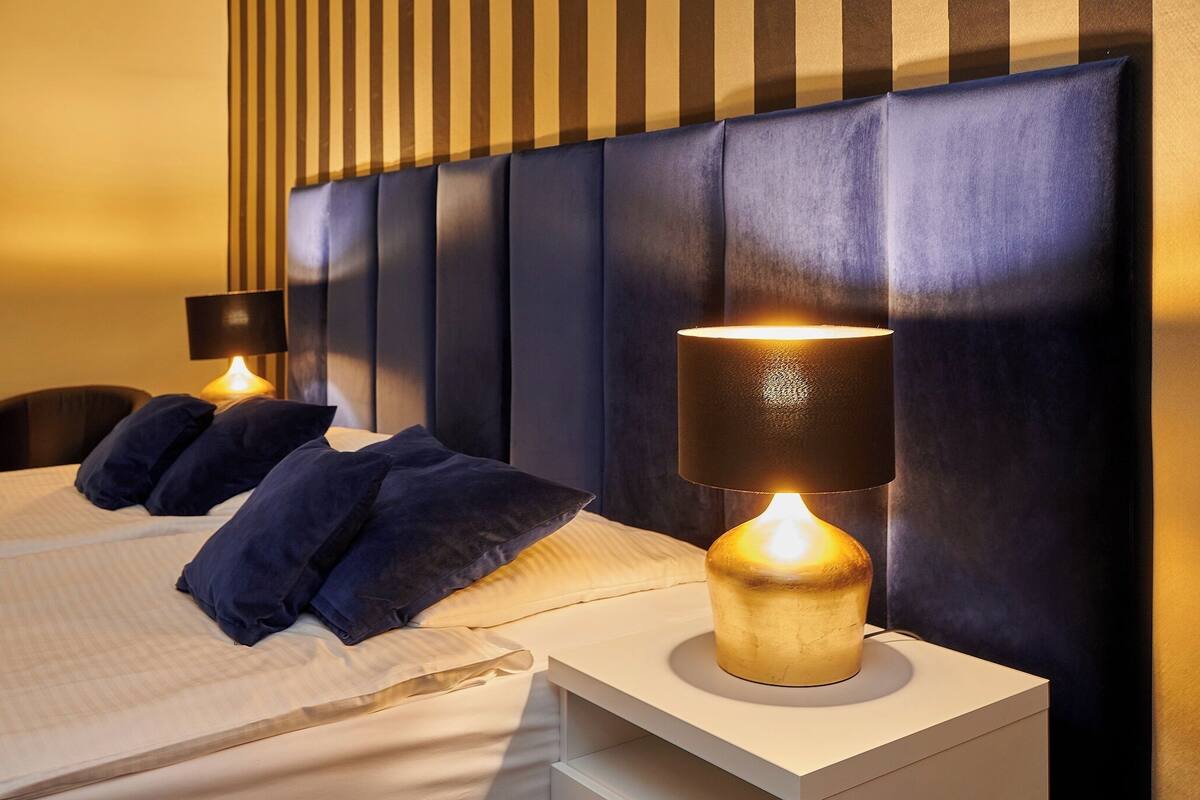 A hotel room with a bed, two bedside lamps, and a striped headboard.