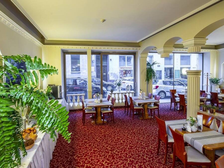 Een hotel lobby met een rood tapijt, eettafels, stoelen en grote ramen met uitzicht op geparkeerde auto's.