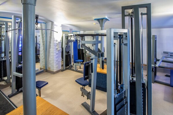 Un gimnasio con diversas máquinas de ejercicio, entre ellas torres de pesas y bancos.
