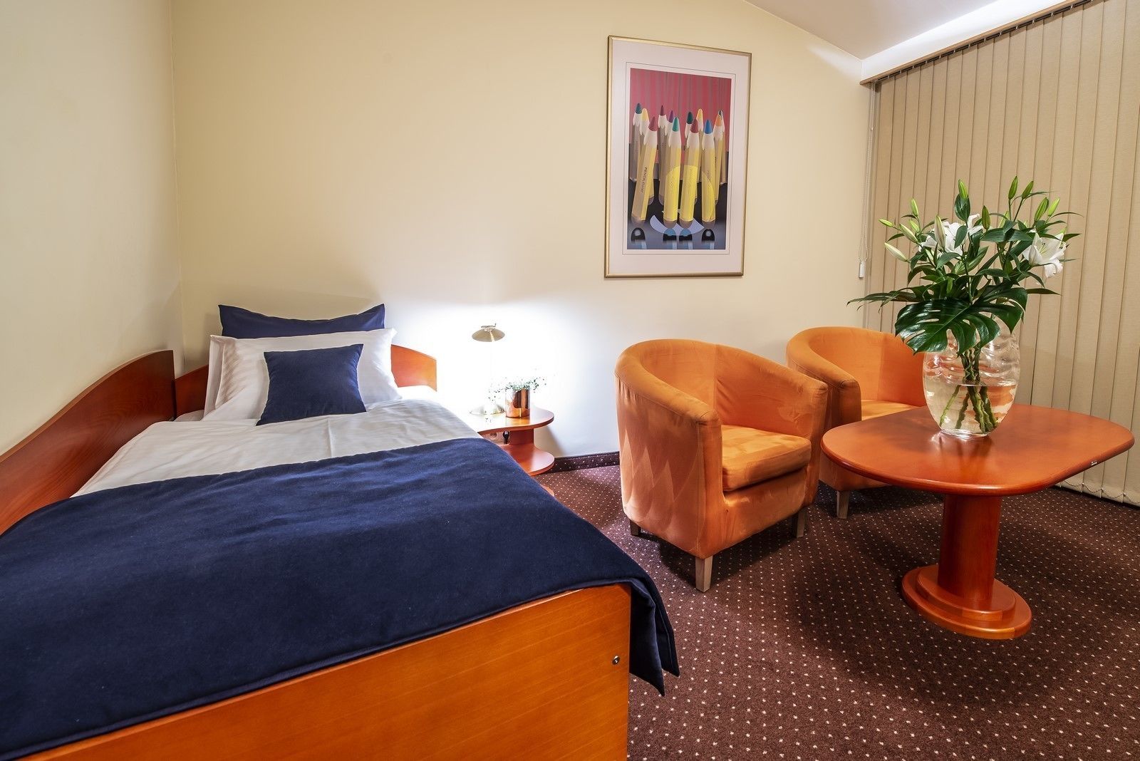 A hotel room with a bed, two armchairs, a small table, a potted plant, and a painting on the wall.