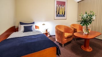 A hotel room with a bed, two armchairs, a small table, a potted plant, and a painting on the wall.
