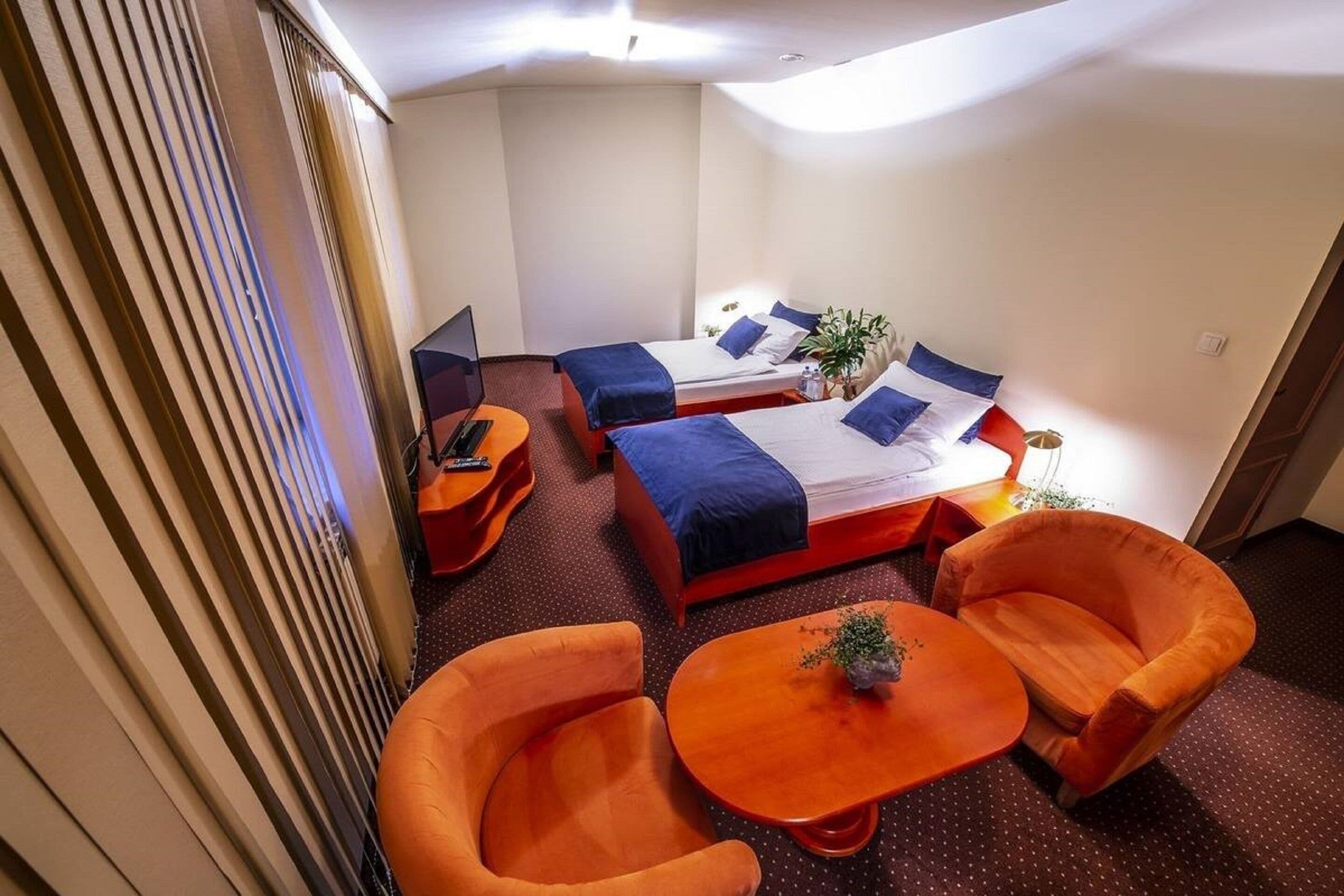 Une chambre d’hôtel avec deux lits, un bureau et deux fauteuils orange.