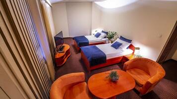 Une chambre d’hôtel avec deux lits, un bureau et deux fauteuils orange.