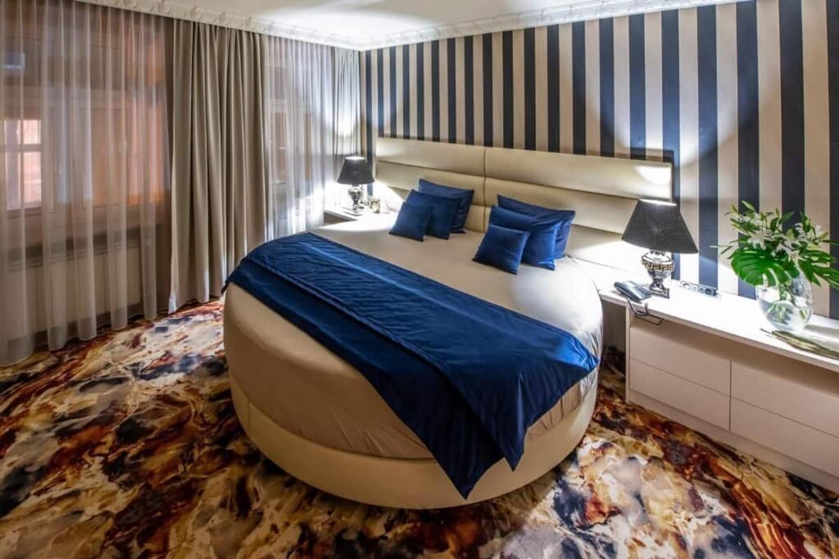A modern hotel room with a round bed, striped wallpaper, and a marble-patterned floor.