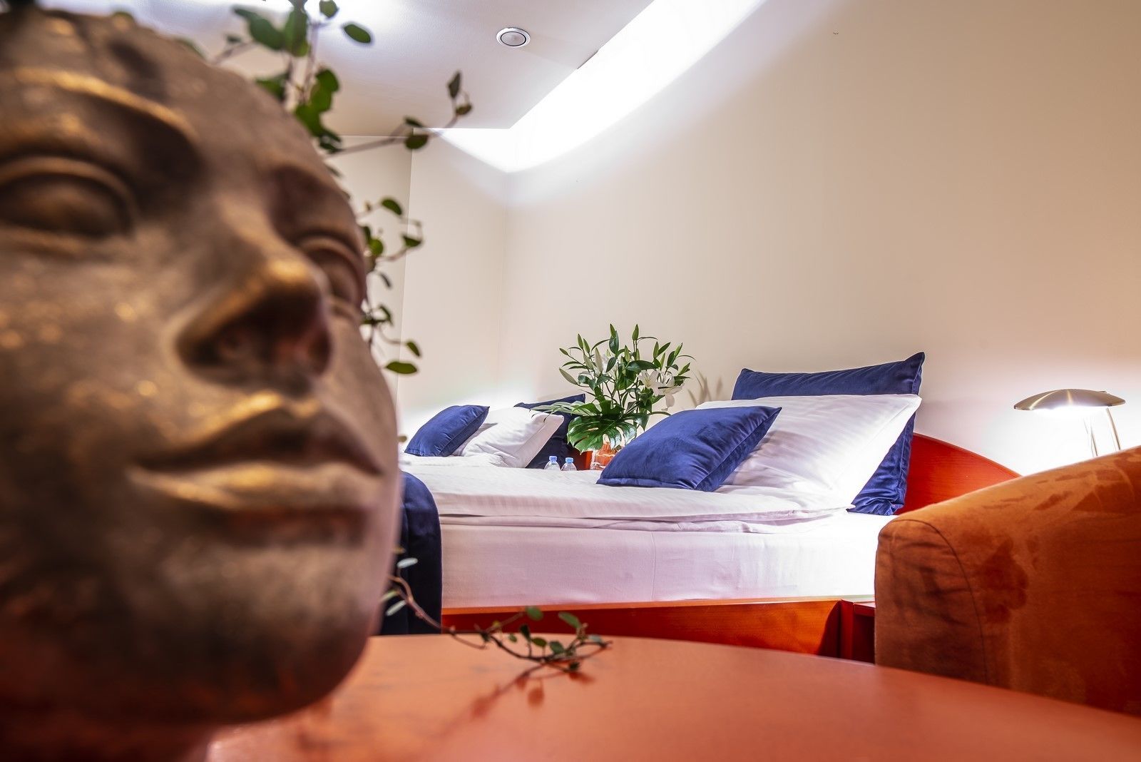 Quarto moderno com cama, travesseiros, planta e uma estátua.