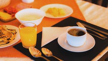 Une table mise pour le petit-déjeuner avec un verre de jus d’orange, une tasse de café et des assiettes remplies de nourriture, notamment des crêpes et des fruits.