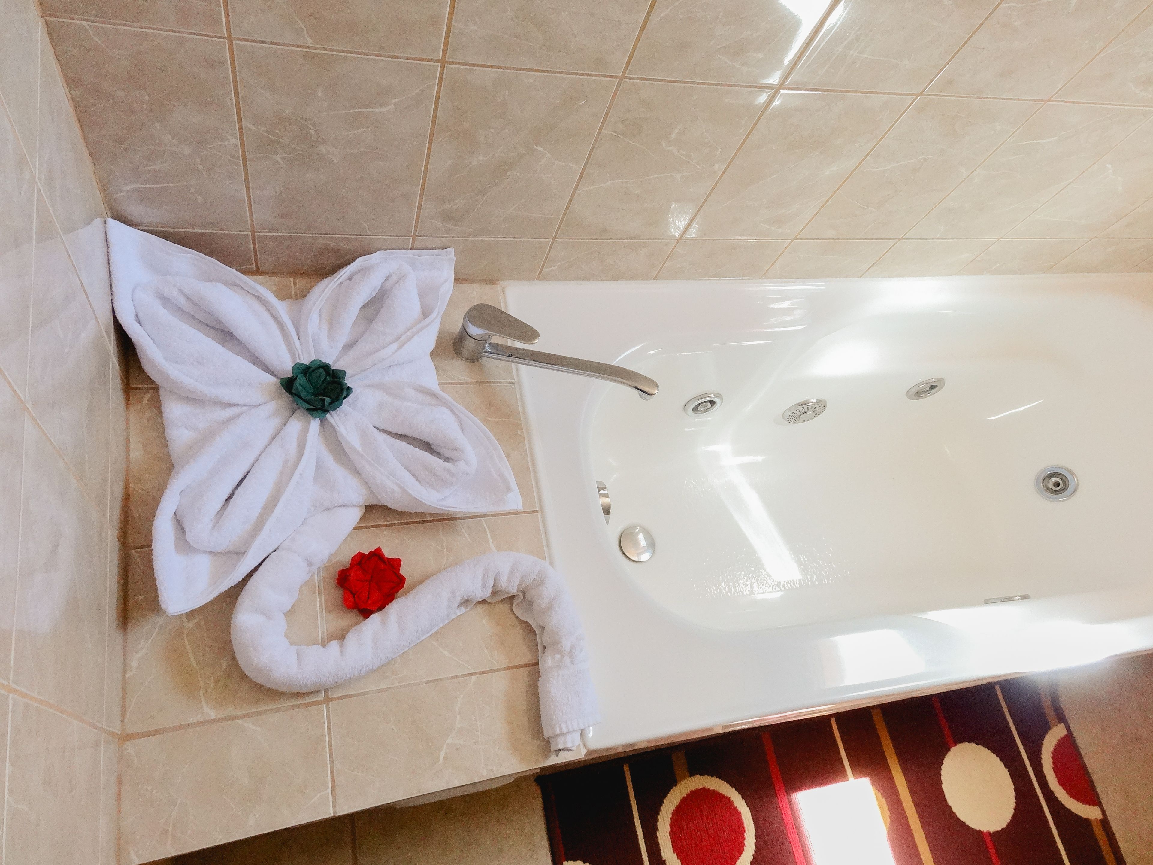 A bathroom with a bathtub, a towel with a green flower, and a red rose.