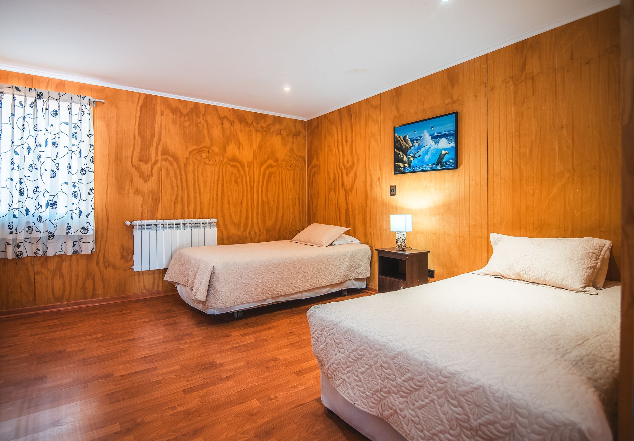 Ett hotellrum med två sängar, träpanel på väggarna, ett element, en tavla och en lampa.