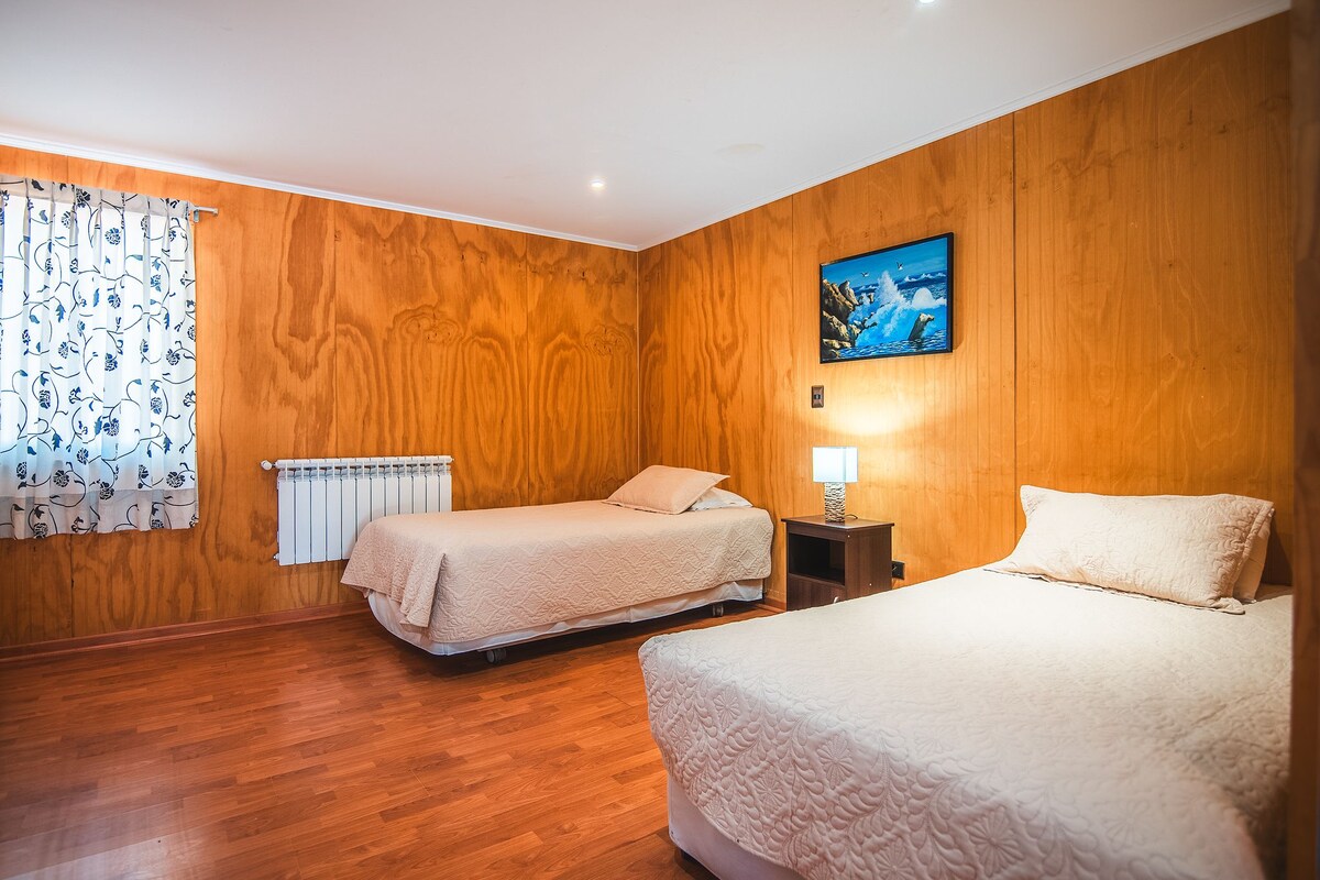 Habitación de hotel con dos camas, paneles de madera, un radiador, un cuadro y una lámpara.