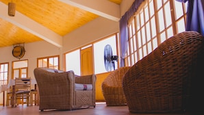 Una habitación amplia con techo alto, ventanas grandes, muebles de mimbre y un comedor.