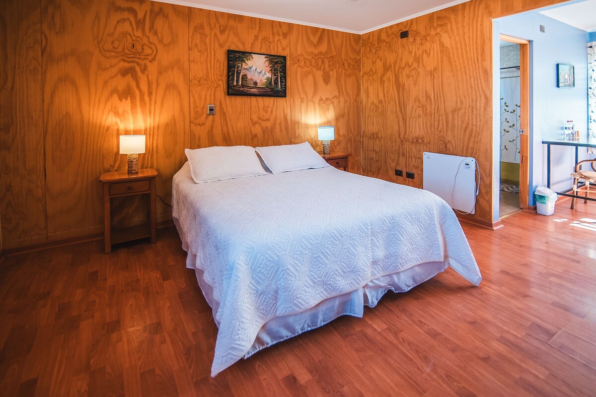 Un dormitorio con suelo de madera, una cama con ropa de cama blanca, dos lámparas de noche y un cuadro en la pared.