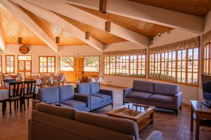 Un espacio interior amplio con vigas de madera, ventanas grandes y arreglos de asientos.