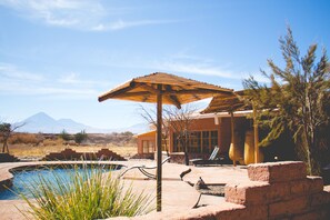Un espace piscine agrémenté d’un parasol en bois, d’une chaise longue et offrant une vue sur les montagnes en arrière-plan.