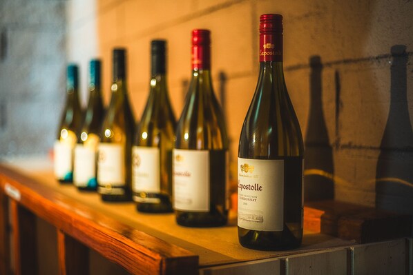 Une rangée de bouteilles de vin est posée sur une étagère en bois, le long d’un mur.