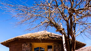 A rustic building with a yellow door, a stone wall, and a tiled walkway leading to the entrance. - Hotel Iorana Tolache (San Pedro de Atacama)