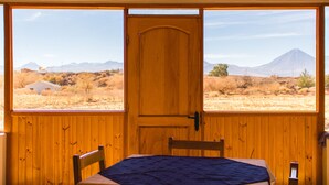 Una habitación con puerta de madera, cama con cubrecama azul y vista a paisaje desértico con montañas.