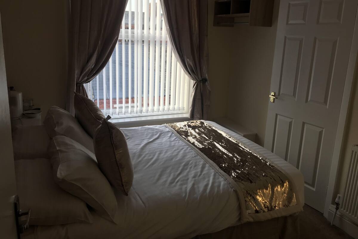 Un dormitorio con cama, cortinas, radiador y puerta.