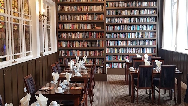 A library with bookshelves, a dining area with tables and chairs, and a chandelier.