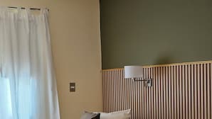 Habitación de hotel con dos camas, una mesita de noche, una lámpara y una ventana con cortinas.