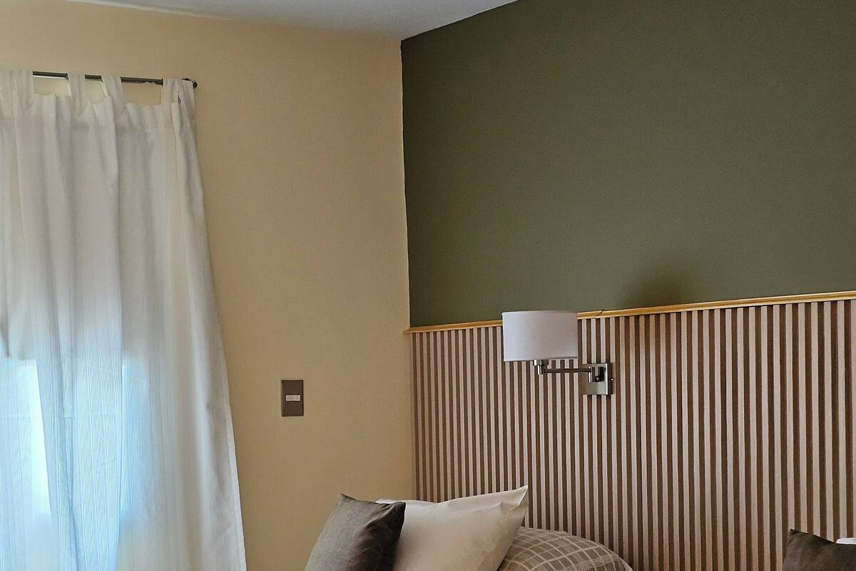 Habitación de hotel con dos camas, una mesita de noche, una lámpara y una ventana con cortinas.