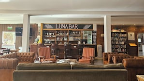 Un área de descanso con sofás de cuero, un bar con diversas bebidas y una estantería llena de libros.