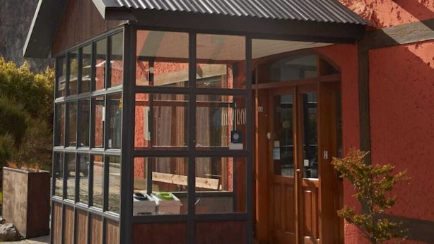 Una casa moderna con fachada roja, un amplio acceso por puerta de cristal y un porche cubierto.