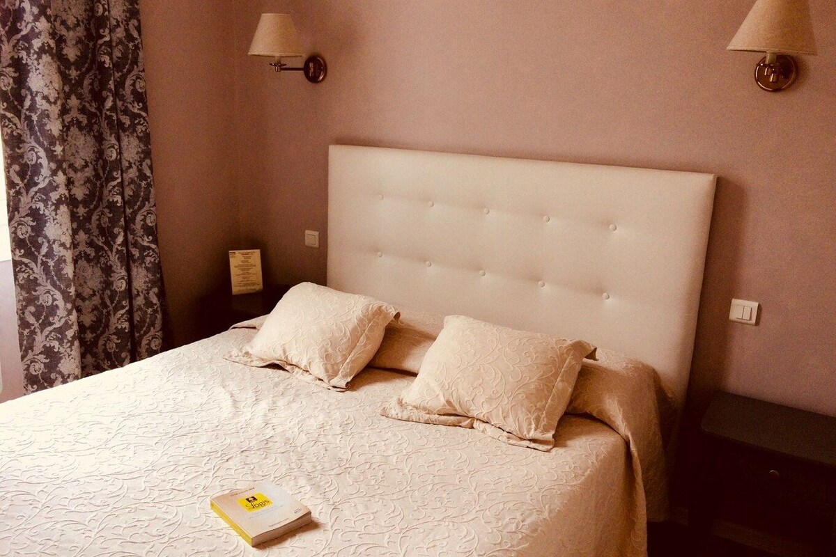 A neatly made bed with a tufted headboard, two pillows, and a book on the bed.
